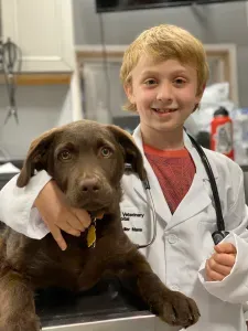 Adler Mann in a white coat with a stethoscope, hugging a chocolate Labrador puppy
