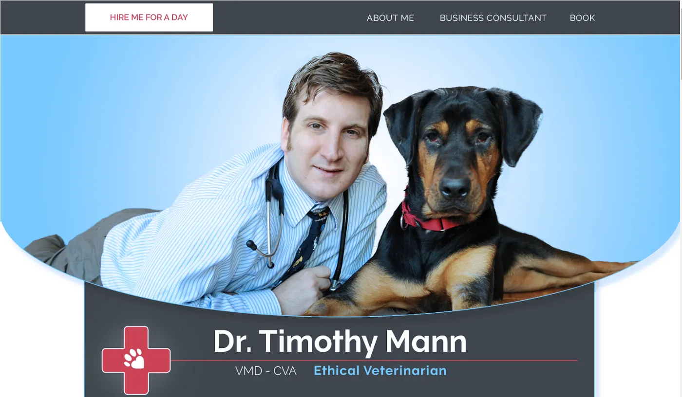 Dr. Timothy Mann, VMD, CVA, in a striped shirt and stethoscope lying beside a black and tan dog in a red collar